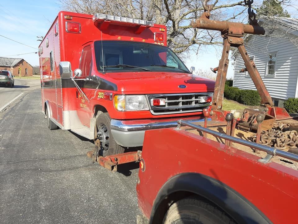 A red ambulance is being towed by a red tow truck