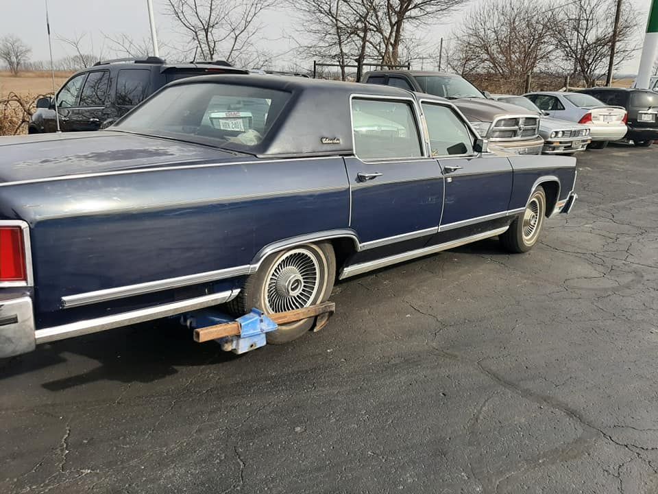 A blue car with a broken tire is parked in a parking lot
