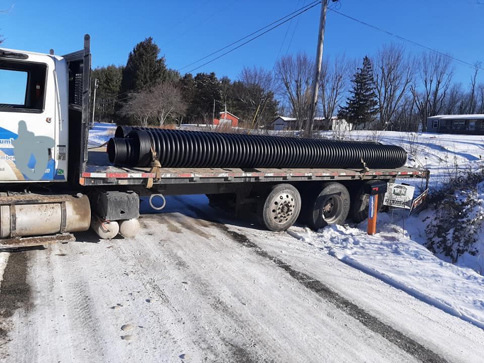 A truck is carrying a large black pipe on a snowy road.