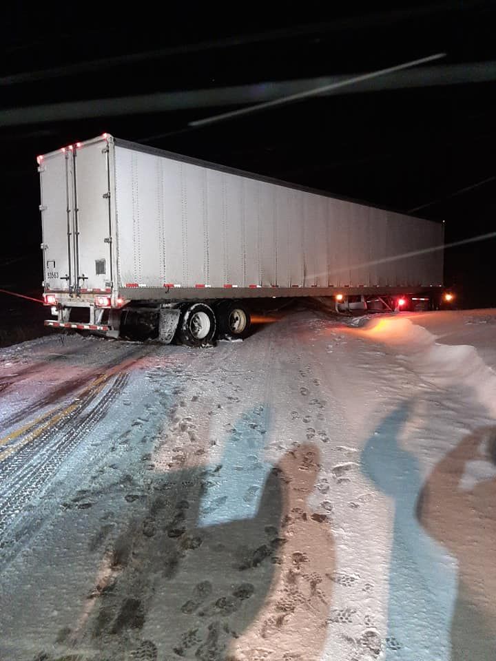 A semi truck is stuck in the snow on a snowy road at night.