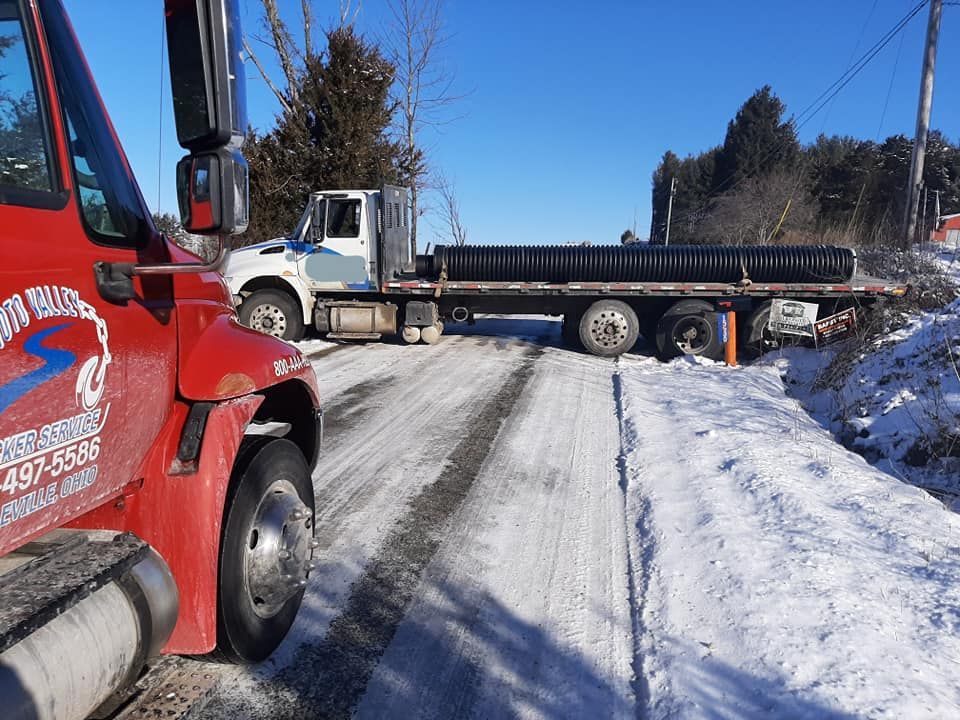 A red tow truck is driving down a snowy road.