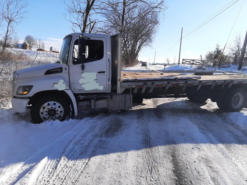 A flatbed tow truck is parked on a snowy road.