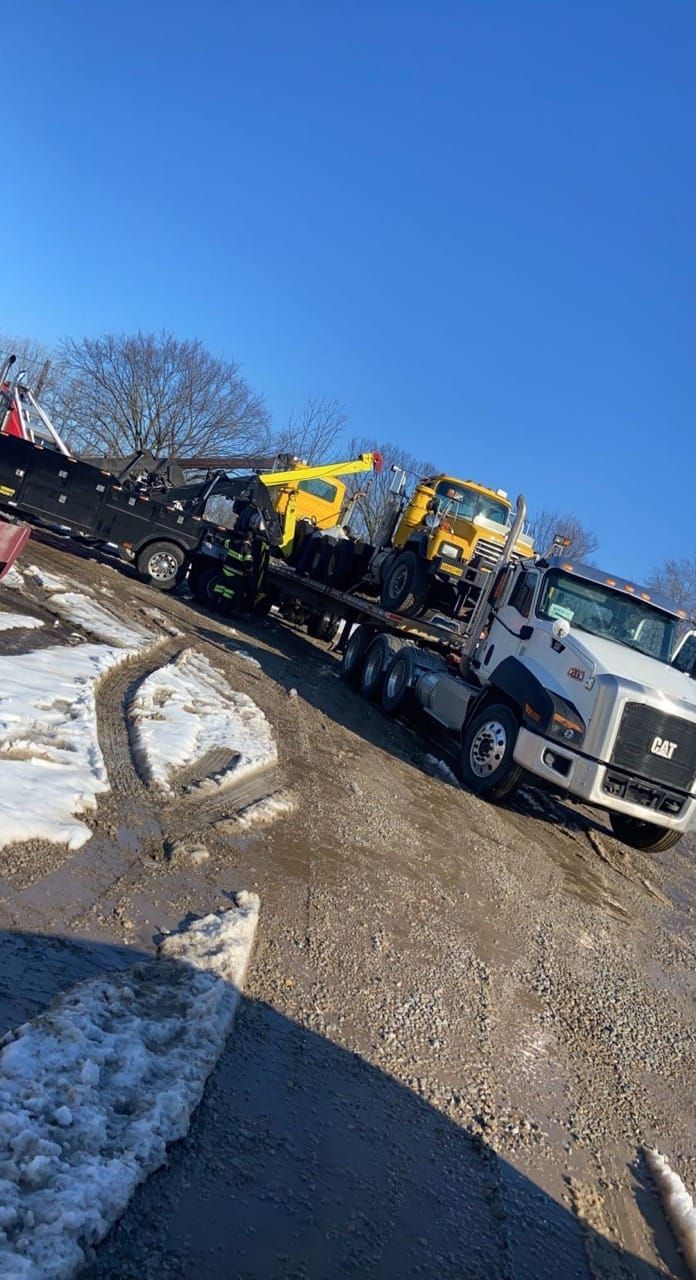 A tow truck is carrying a yellow tractor on a flatbed trailer.