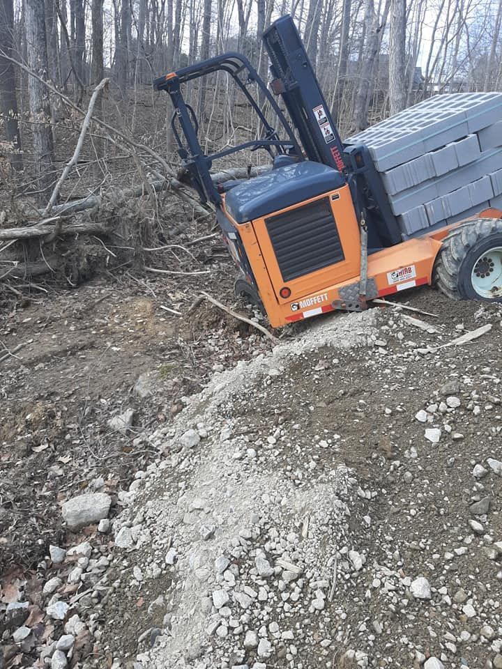 A forklift is stuck in the dirt in the woods.
