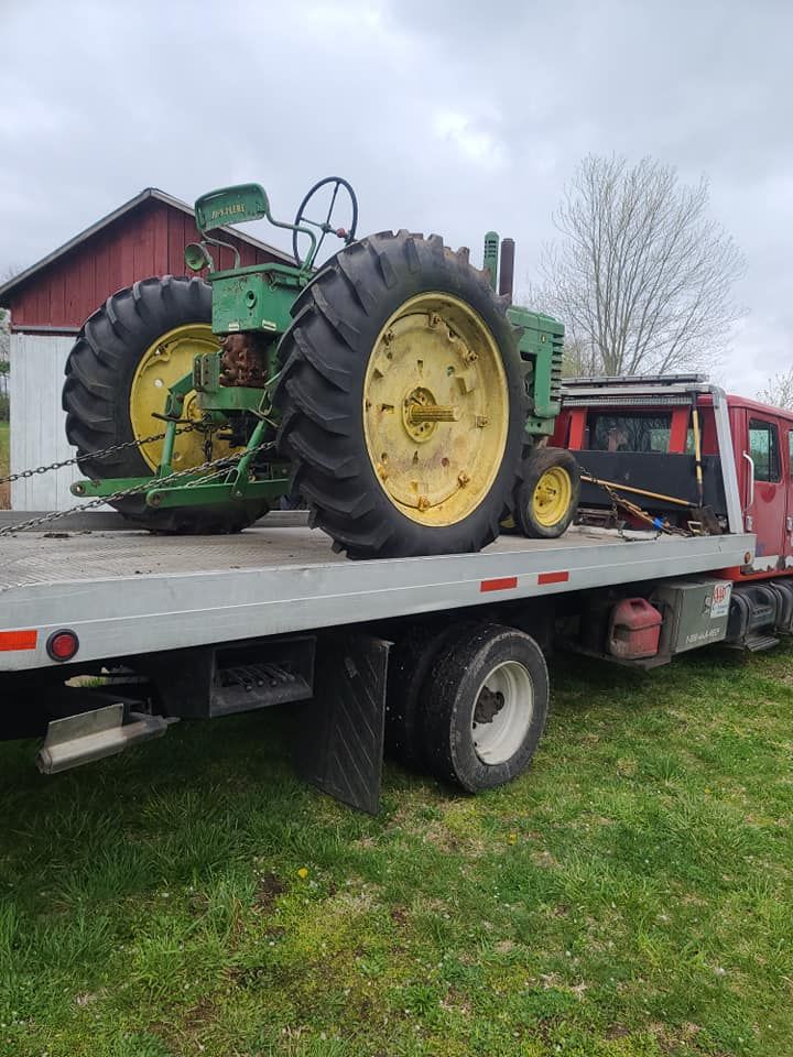 An old john deere tractor is being towed by a tow truck.