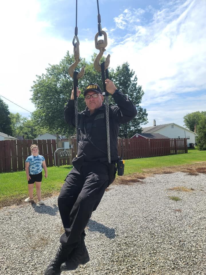 A man is sitting on a rope swing with a girl standing behind him