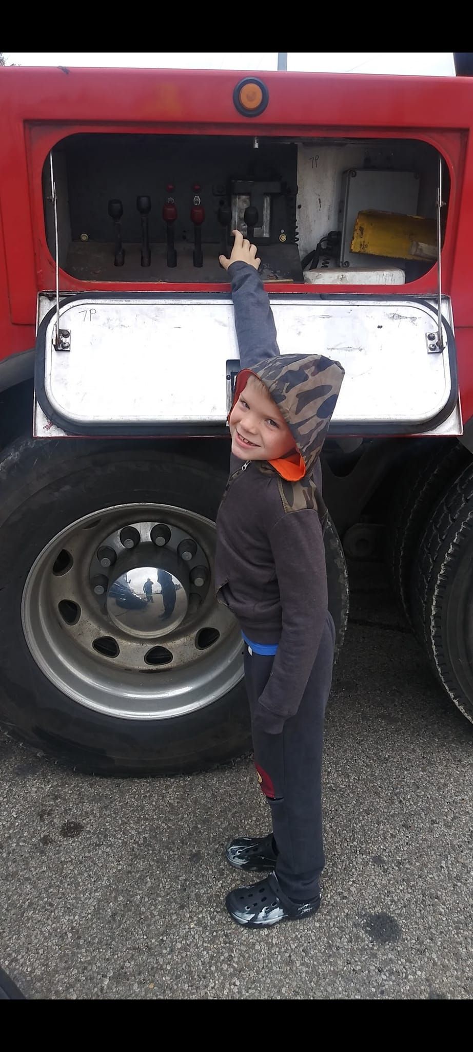 A little boy is standing in front of a red truck.