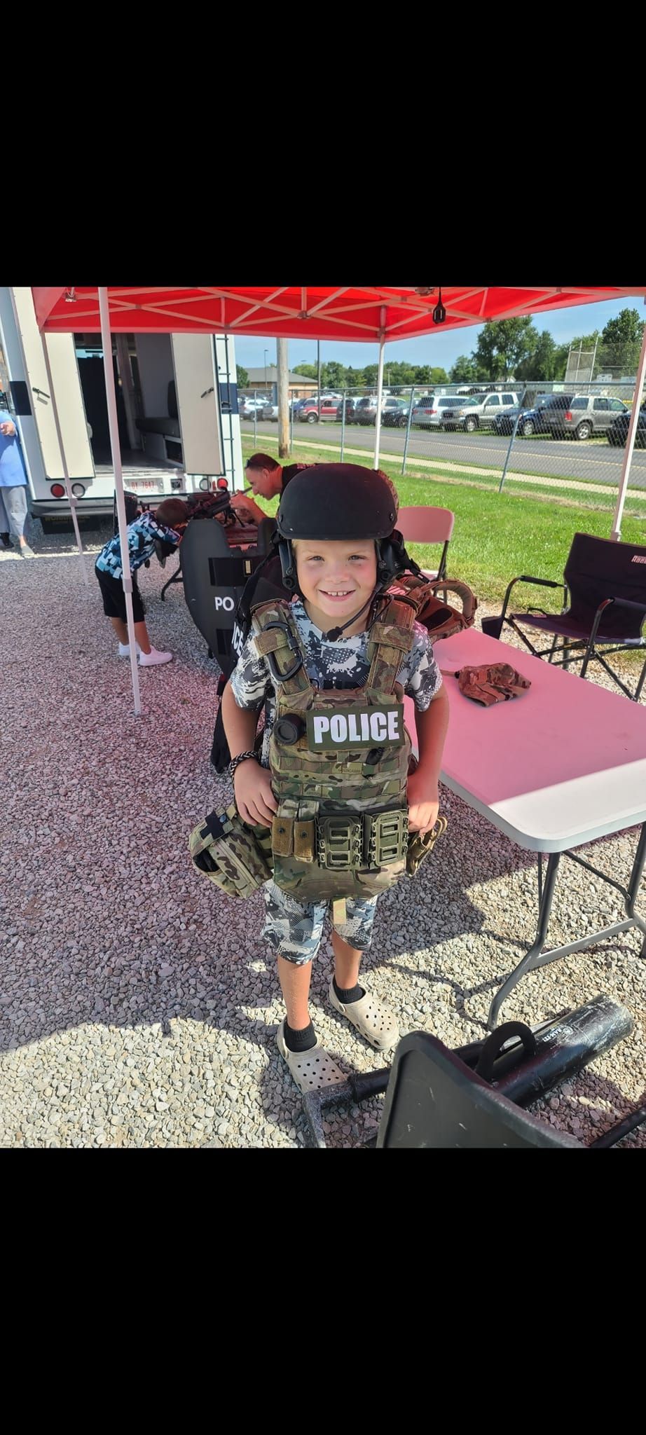 A little boy in a military uniform is standing in front of a tent.