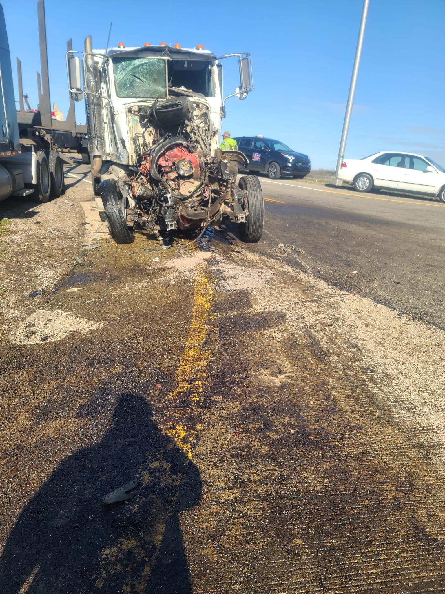A shadow of a person is cast on the ground in front of a damaged truck