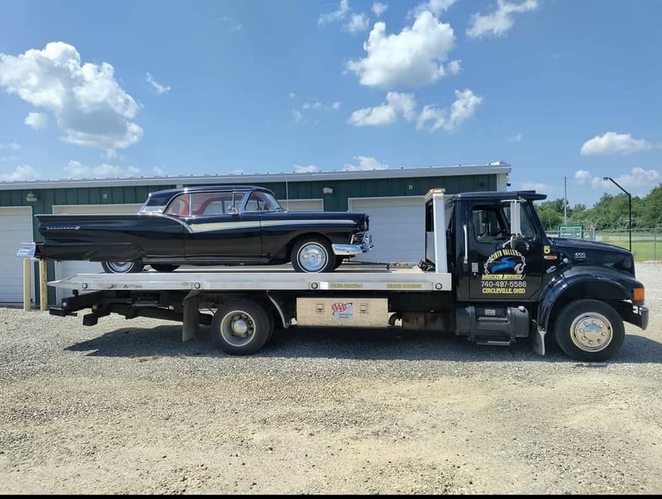 A tow truck is carrying a black car on the back of it.
