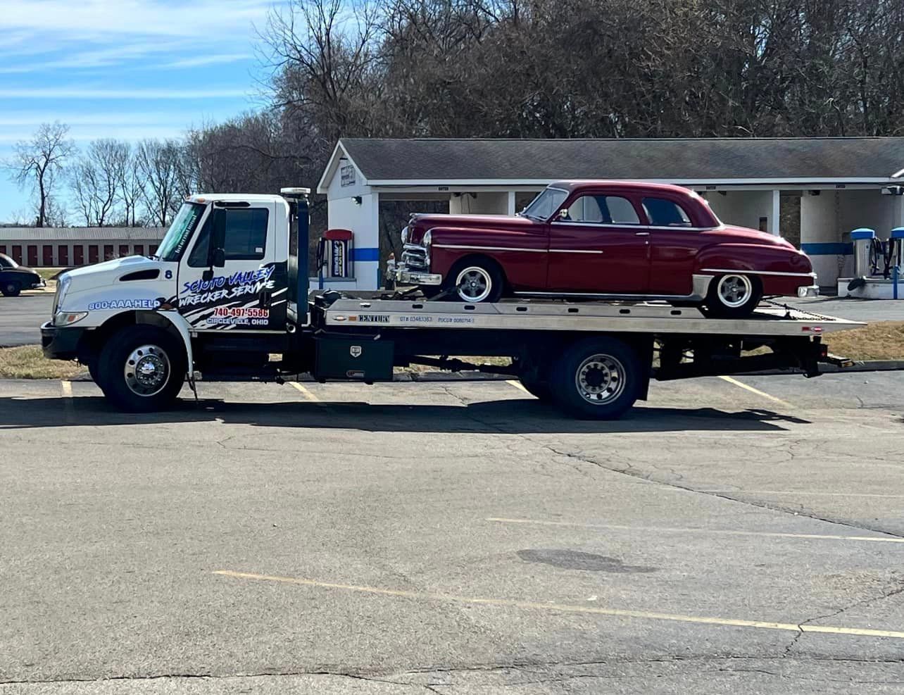 A tow truck with a red car on the back is parked in a parking lot.
