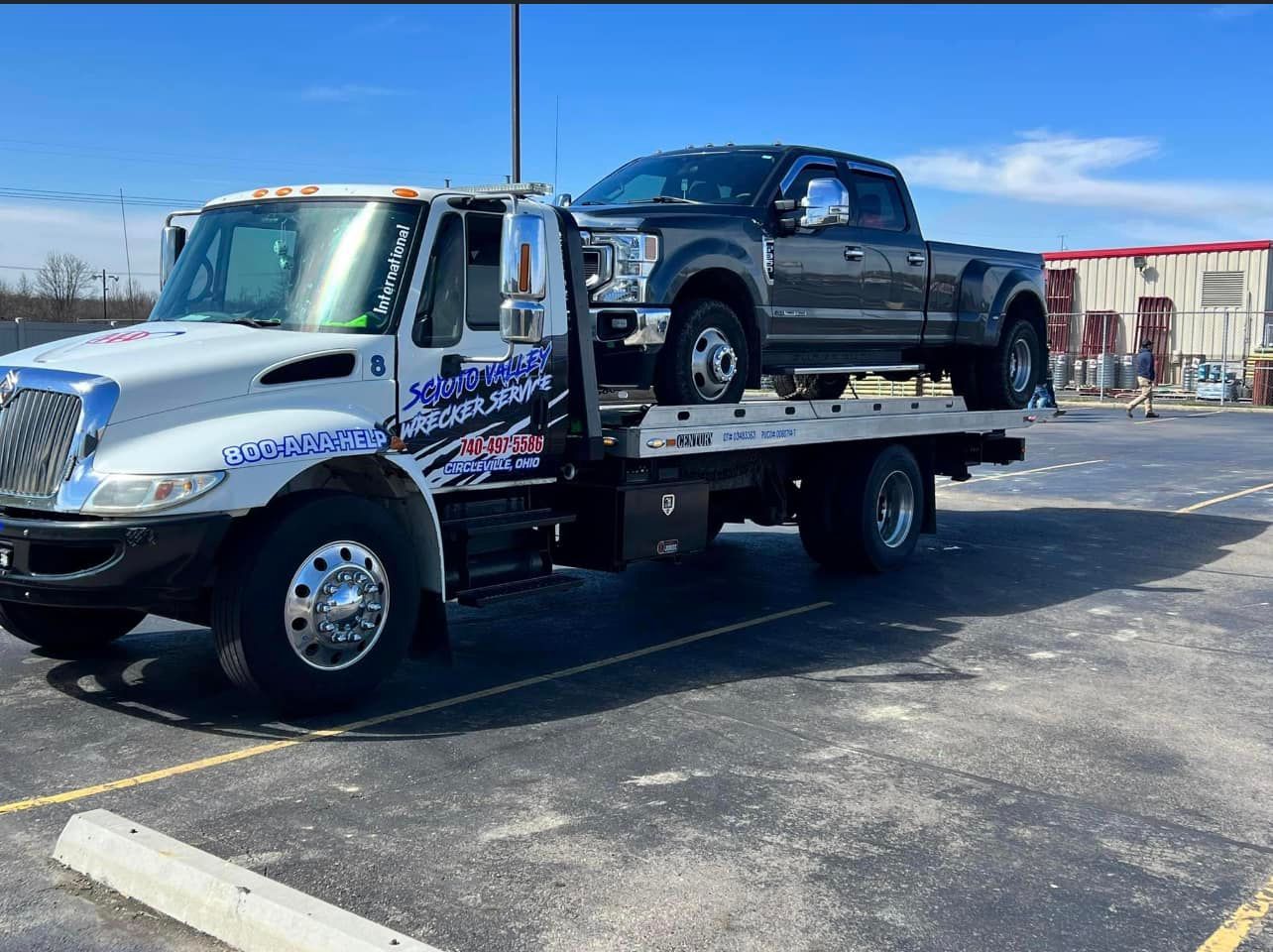 A tow truck is towing a pickup truck in a parking lot.