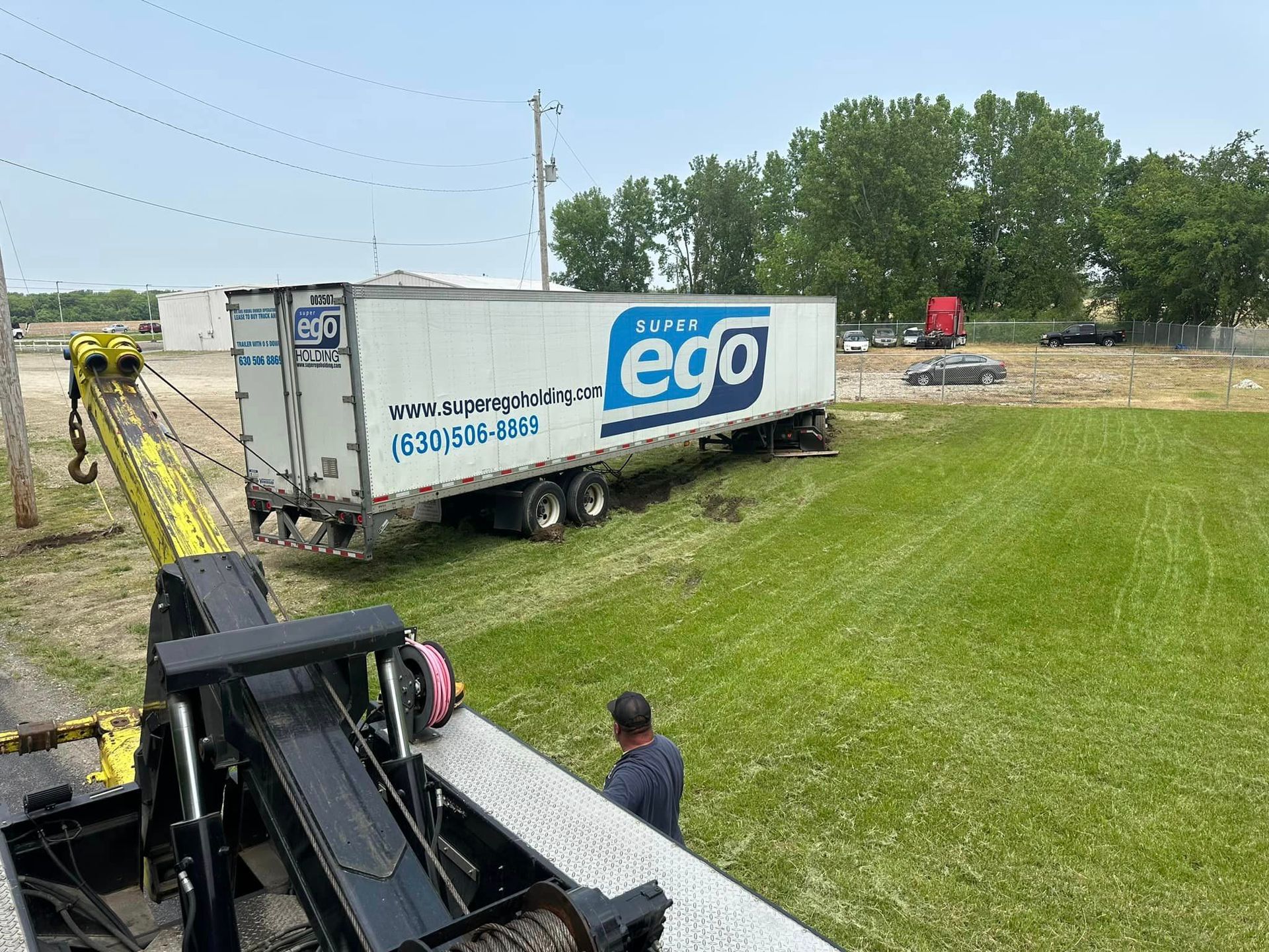 A semi truck is being towed by a tow truck in a grassy field.