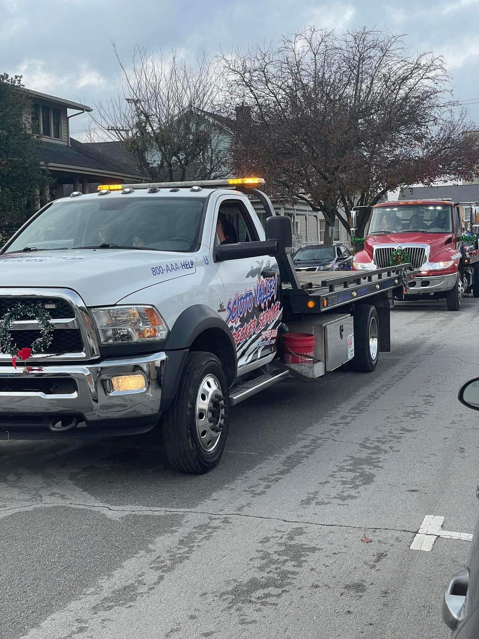 A white tow truck is parked on the side of the road next to a red truck.