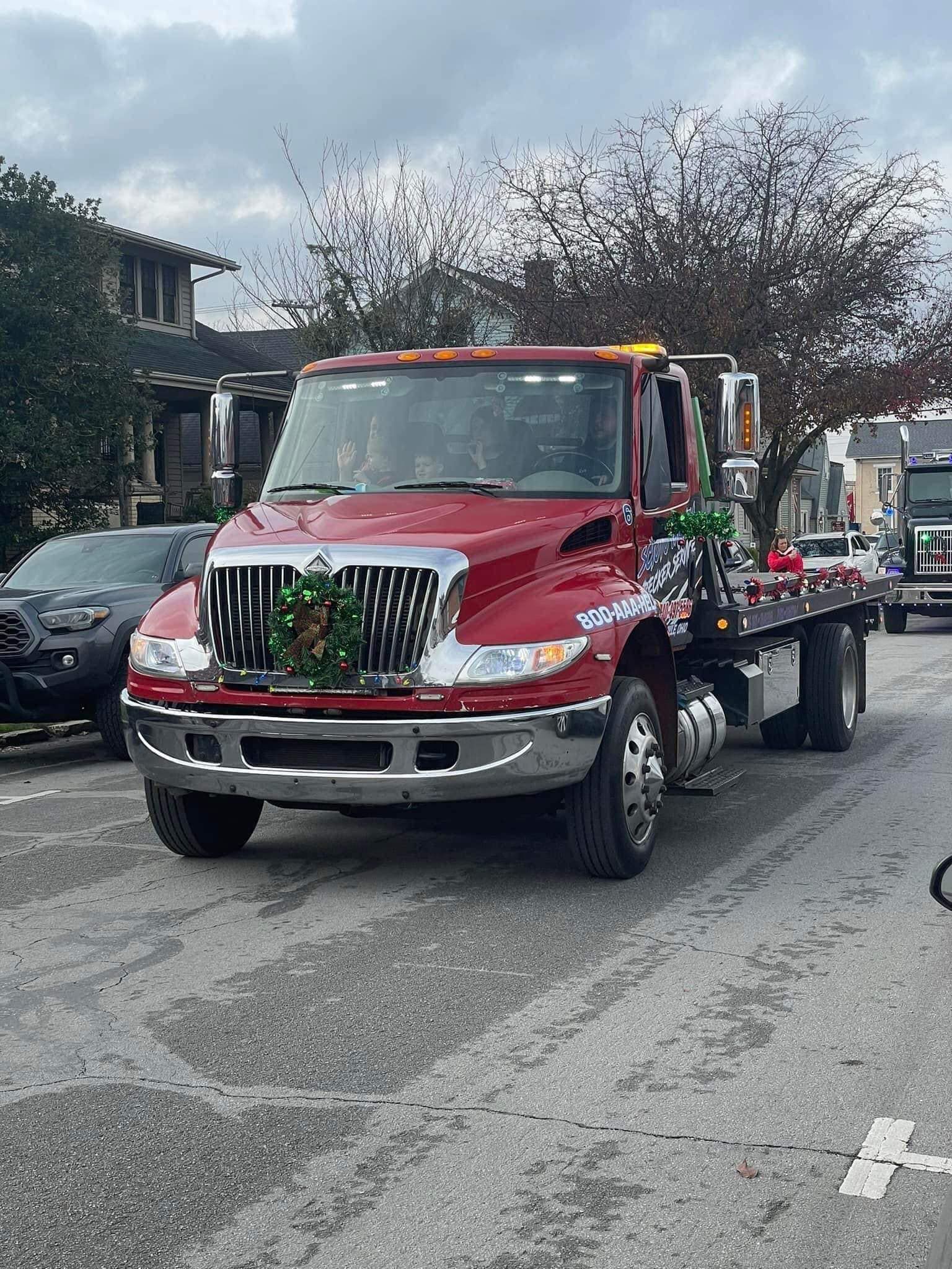 A red tow truck is driving down a street decorated for christmas.