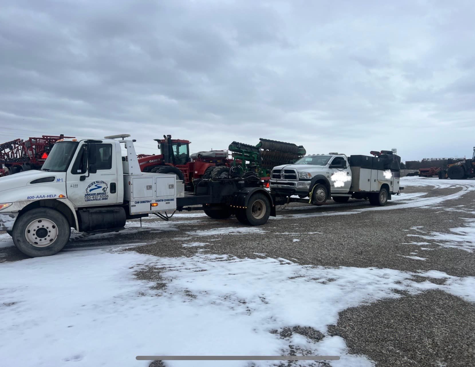 Three tow trucks are parked in a snowy field.
