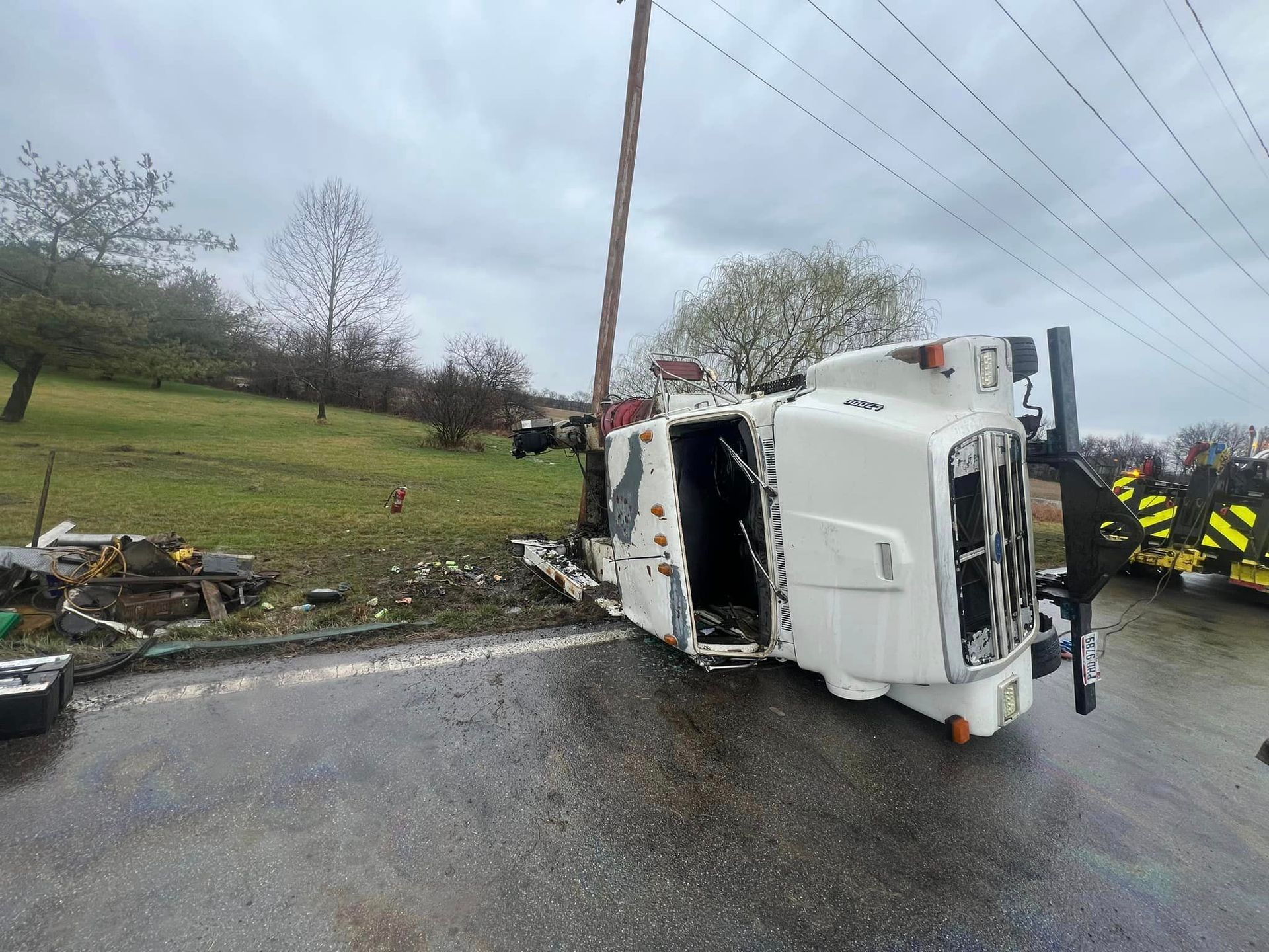 A white truck is turned over on its side on the side of the road.
