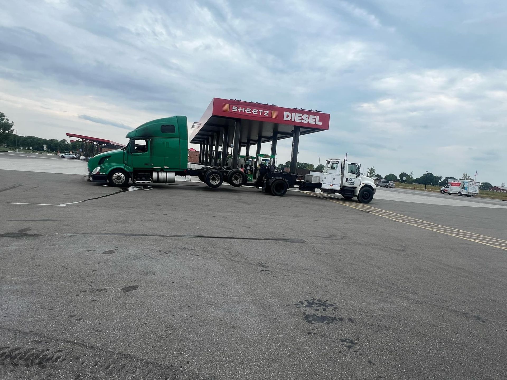 A green semi truck is parked in front of a gas station.