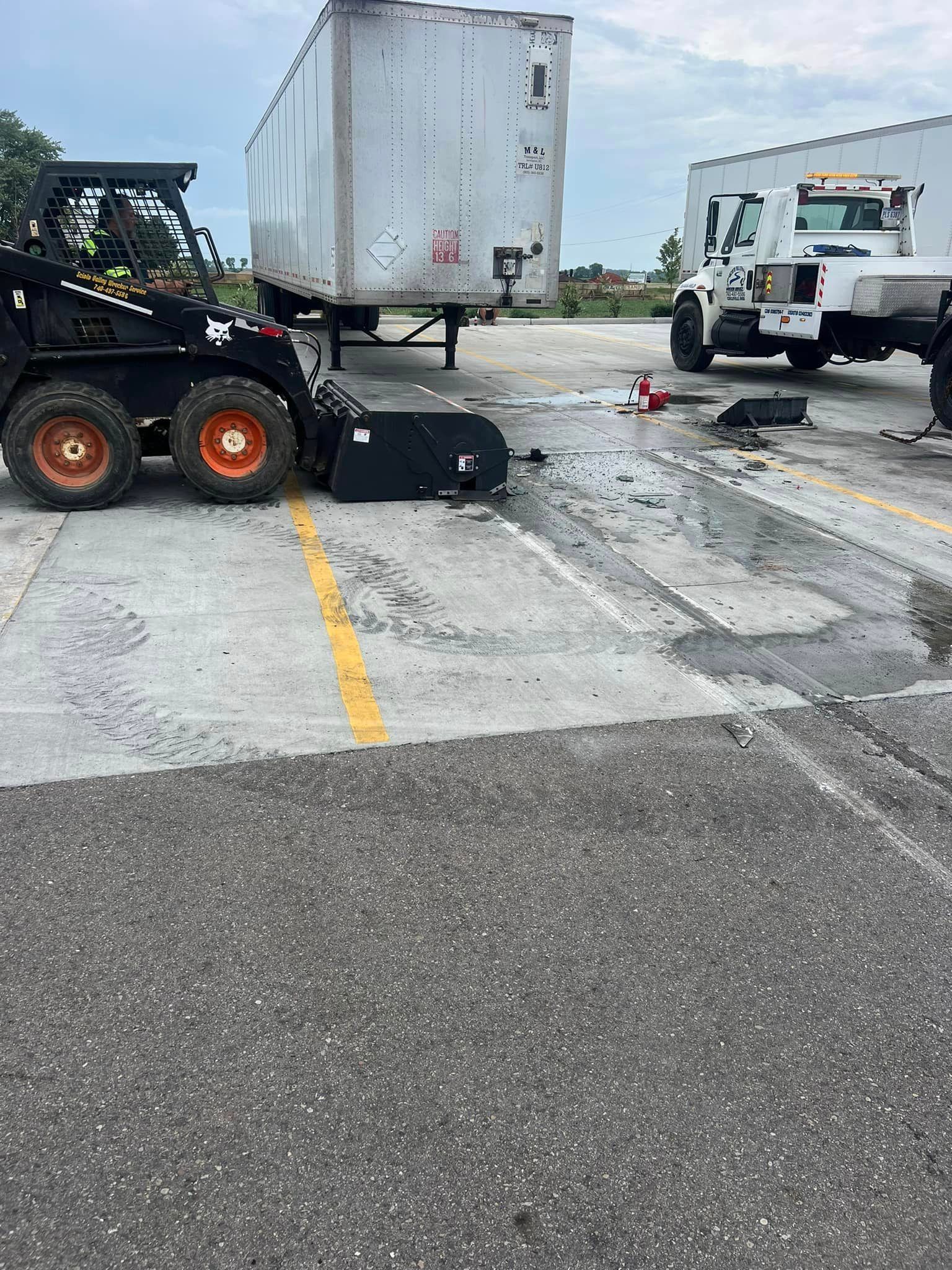 A bulldozer is parked in a parking lot next to a semi truck.