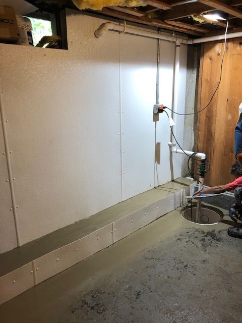 Concrete basement floor with a long drain along the wall and exposed utility panels.