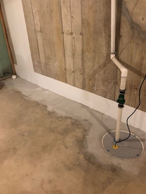 Basement utility area with concrete floor, exposed wall, and a pipe leading to a floor drain.
