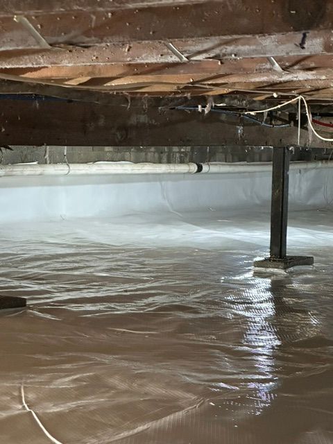 Crawlspace with white plastic vapor barrier on the floor and exposed wooden beams overhead.