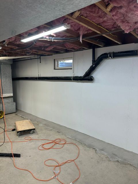 Basement utility area with a floor drain cover, PVC pipe, and coiled black and yellow cables.