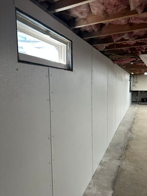 Bare basement wall with small window, exposed ceiling joists, and a long hallway.