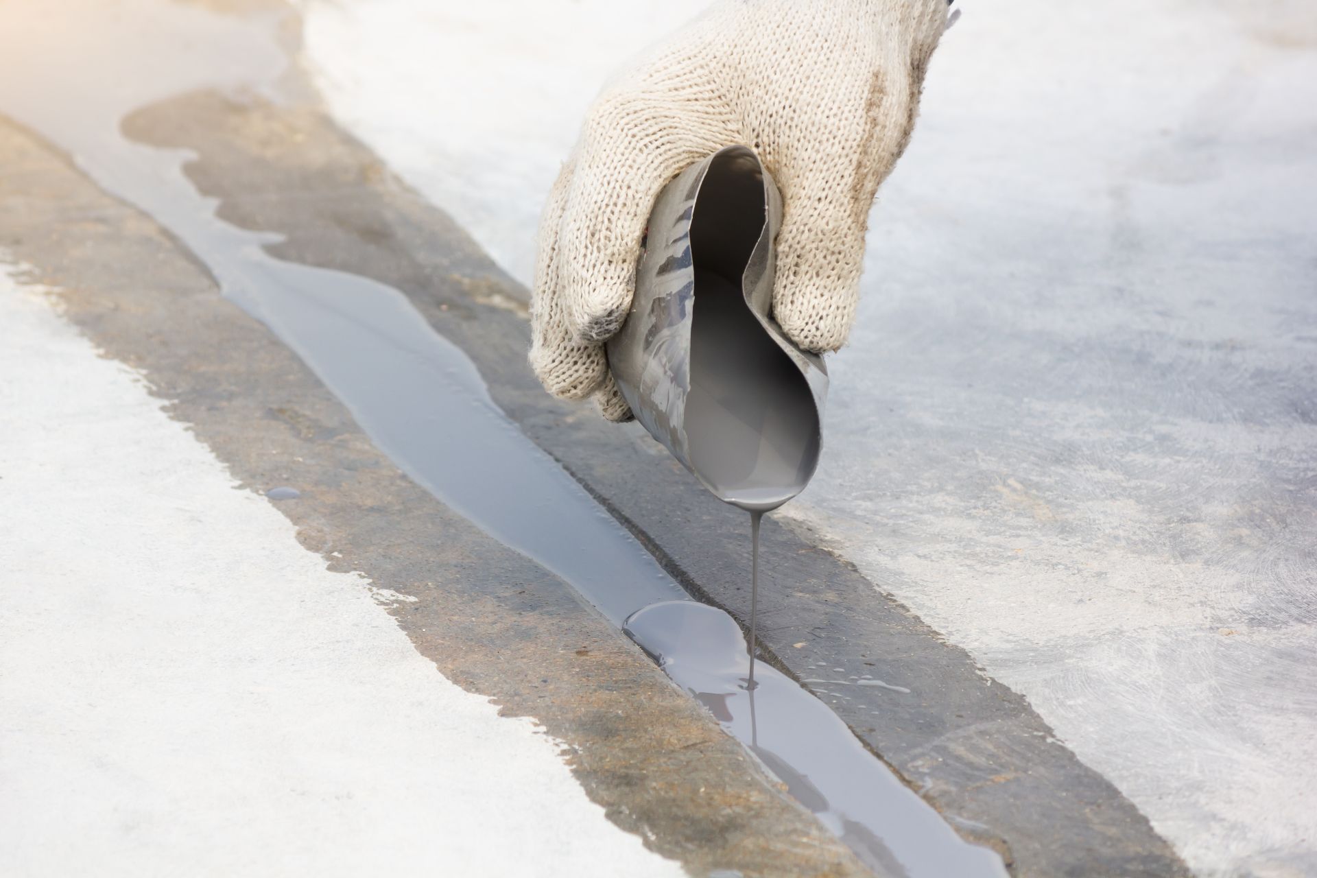 White gloved hand pouring dark liquid onto a concrete surface, forming a thin line.