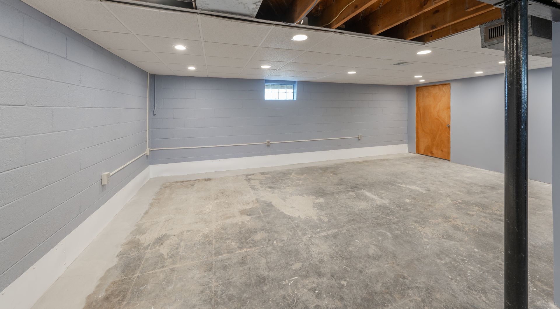 Basement utility area with pipes, coiled hose, and a black machine on a concrete floor.