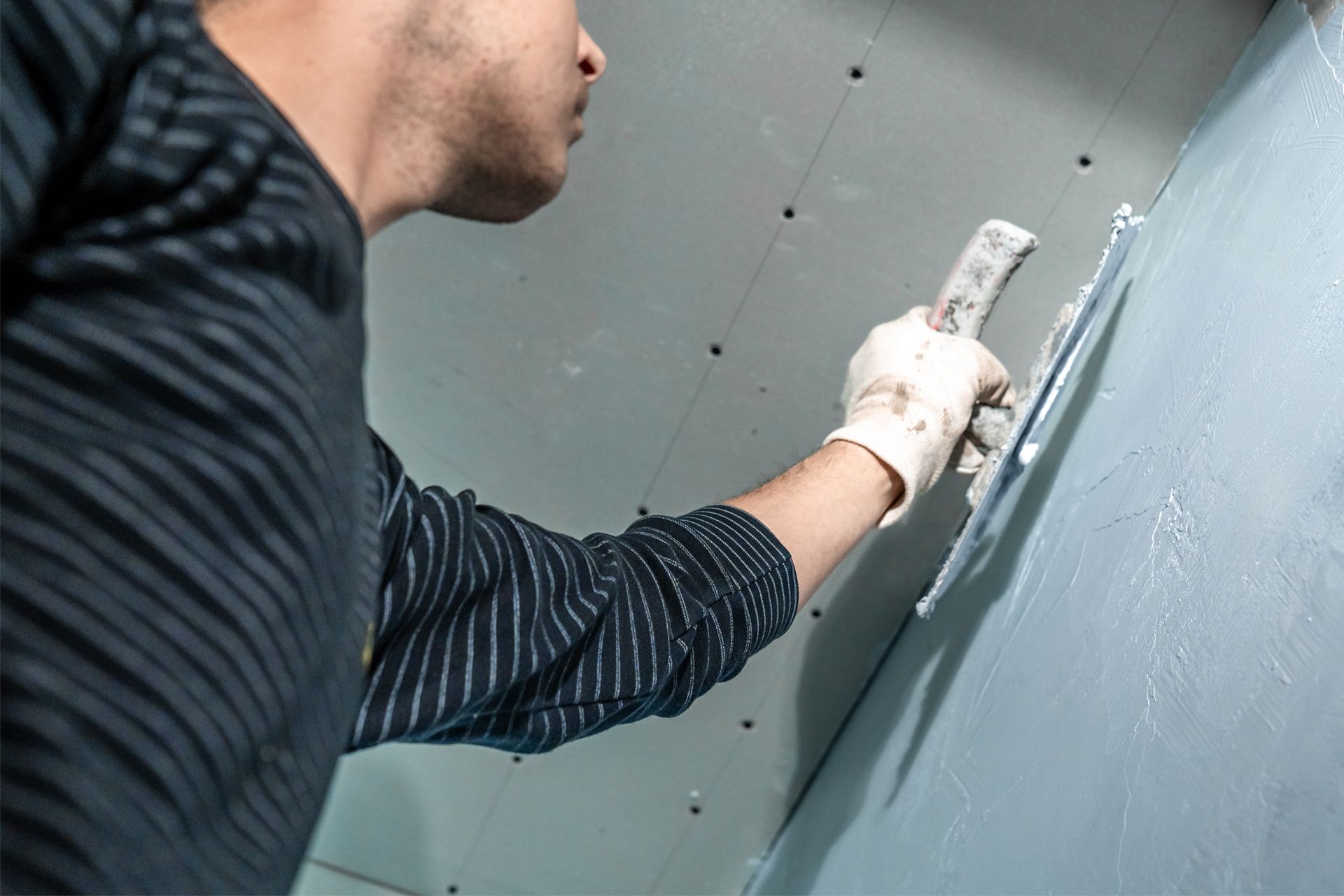 Person in white gloves applying sealant to a blue wall with a putty knife