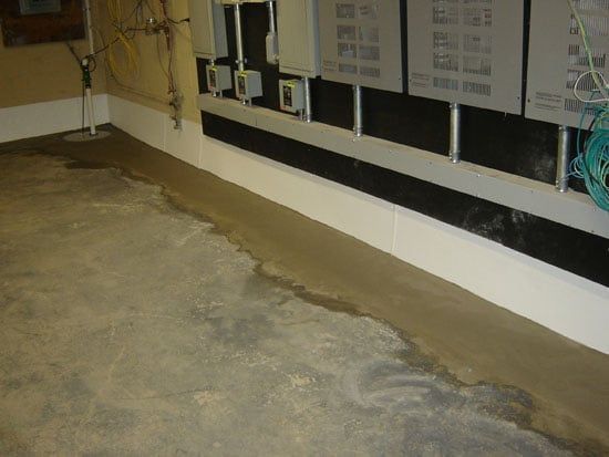 Concrete basement floor with a long drain along the wall and exposed utility panels.