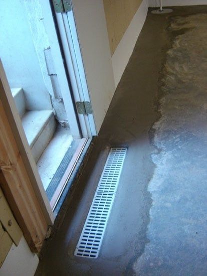 Basement floor with a long white drain beside a doorway, wet concrete around it