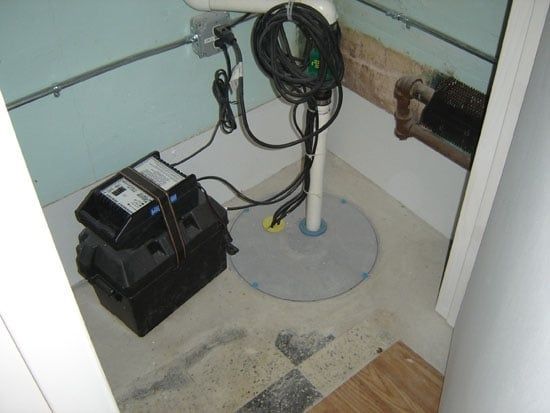 Basement utility area with pipes, coiled hose, and a black machine on a concrete floor.