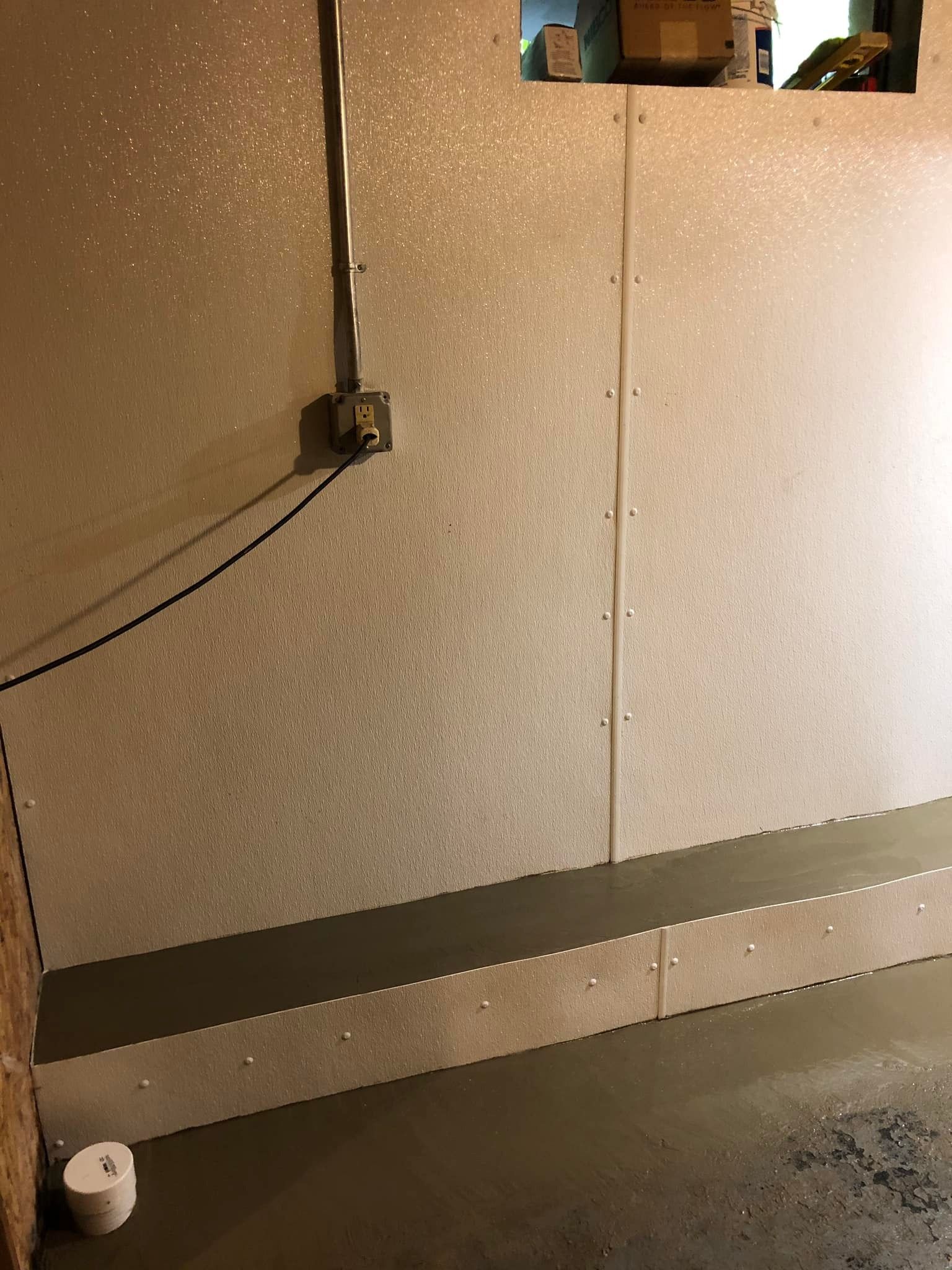 Basement wall with exposed cable, gray paneling, and a small white object on the floor.