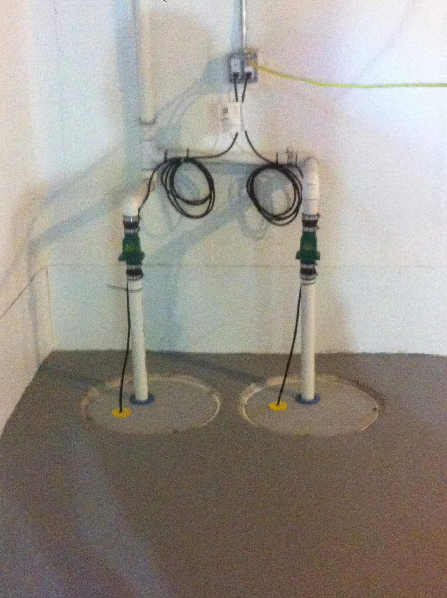 Two vertical white poles with coiled black cables against a wall on a gray floor.