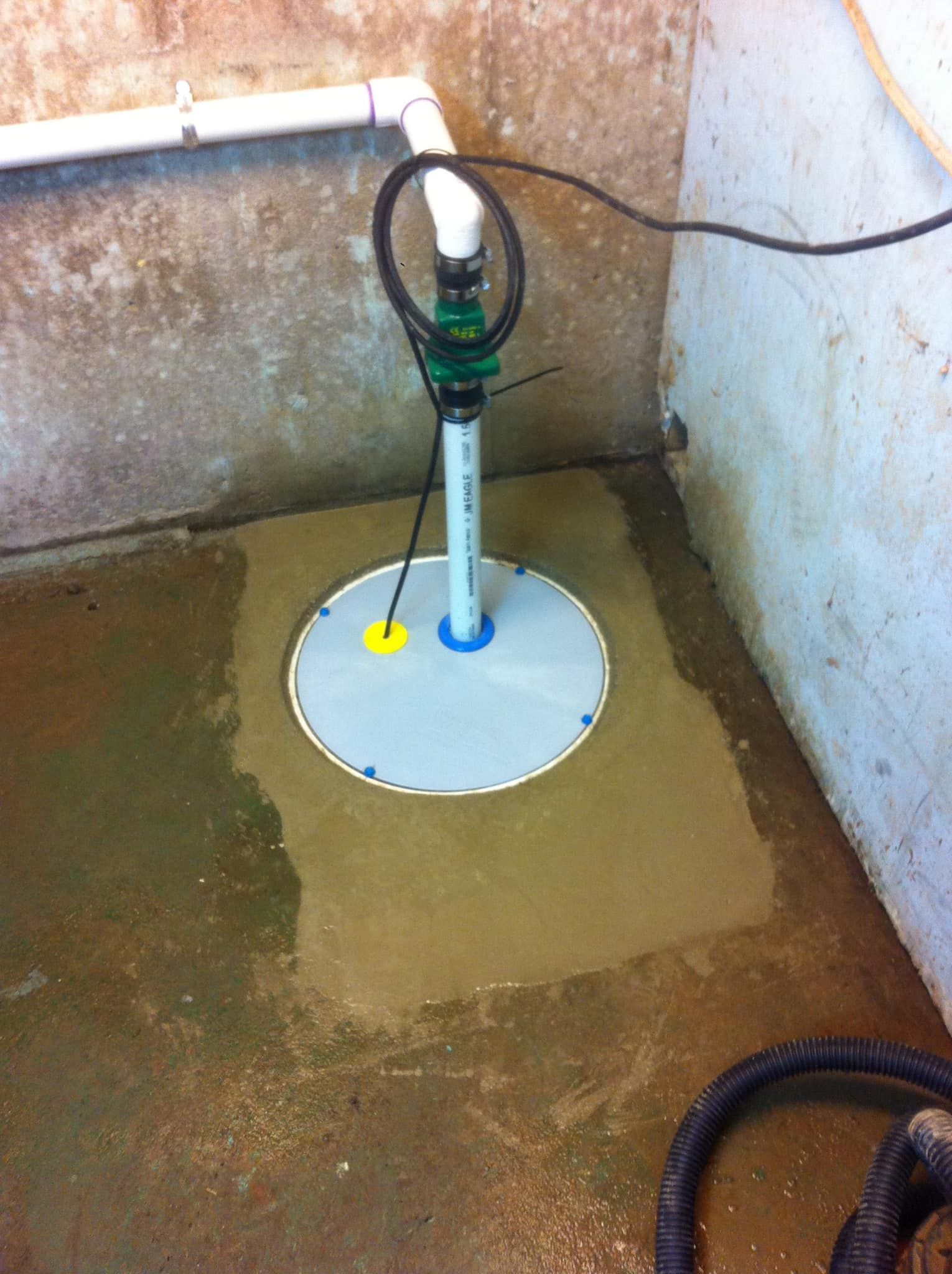 Small utility fixture on a wet concrete floor in a corner, with pipes and a white circular base.