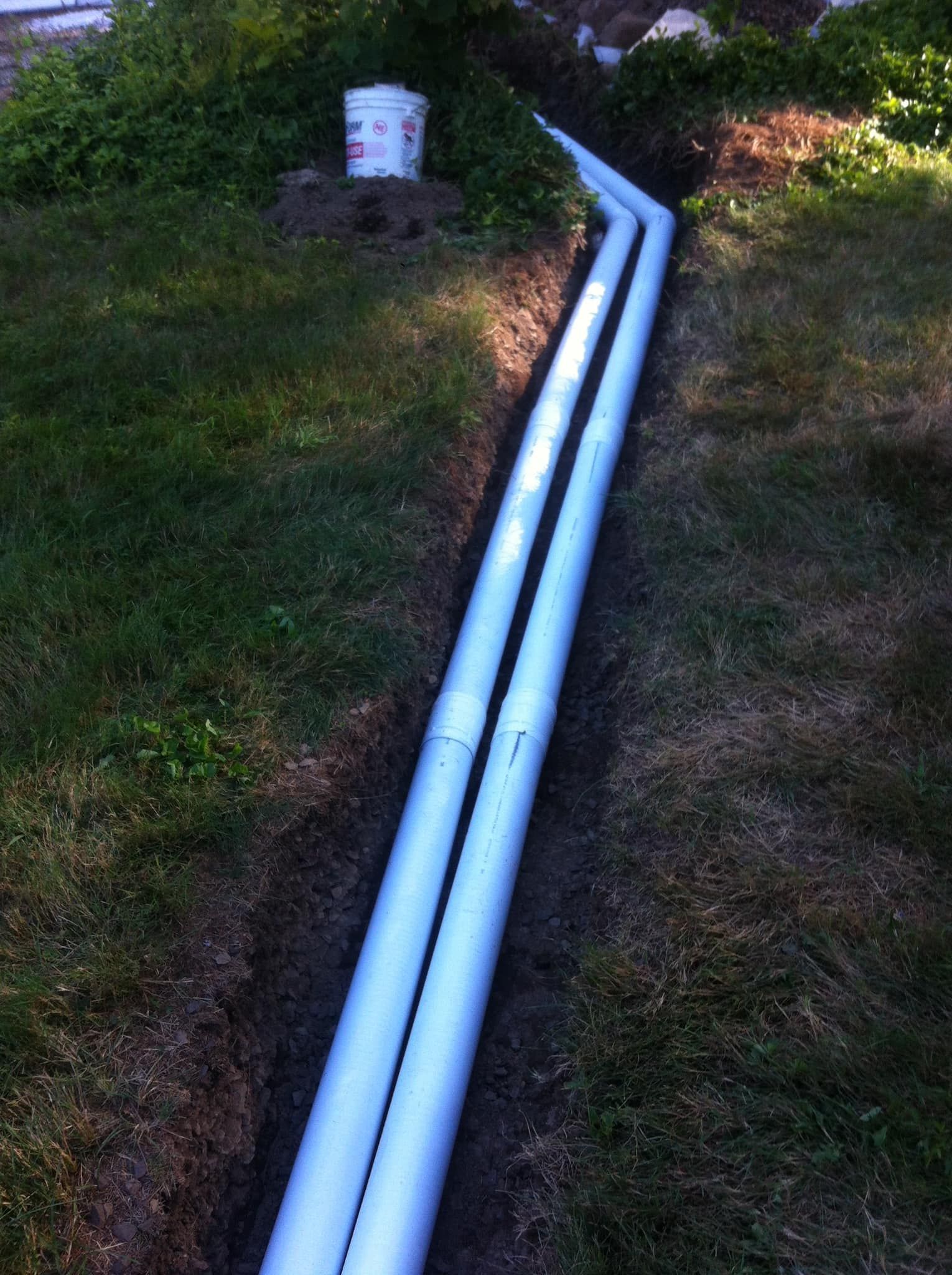 Two white PVC pipes running along a grassy slope toward a utility box.