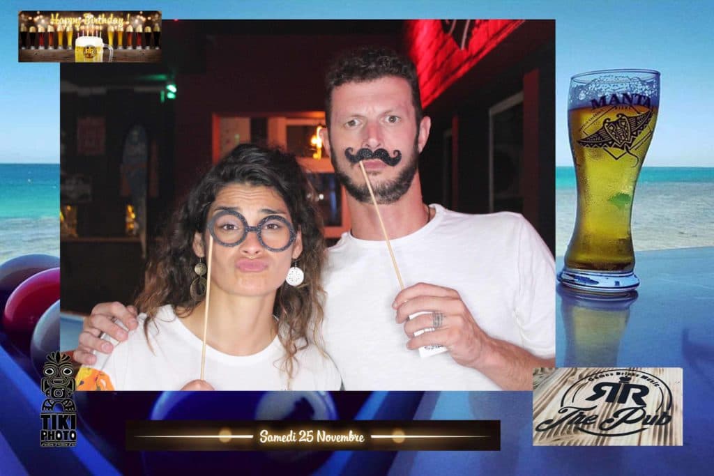 A man and a woman are posing for a picture with a glass of beer in the background.