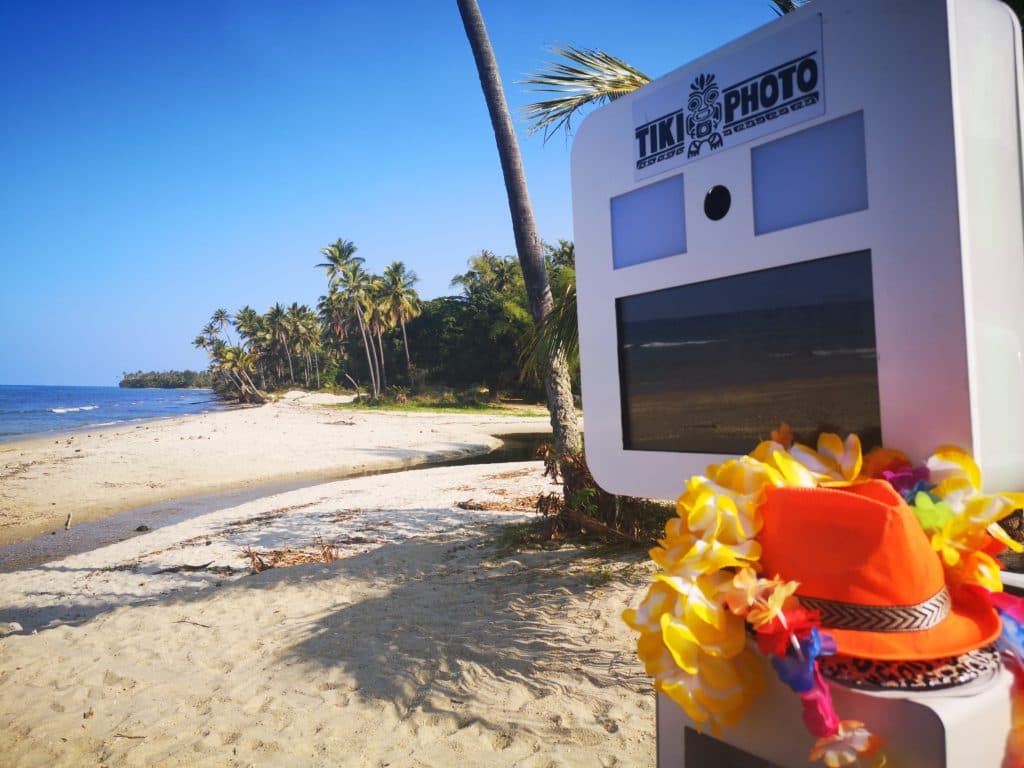 A tiki photo booth is sitting on the beach next to a palm tree.