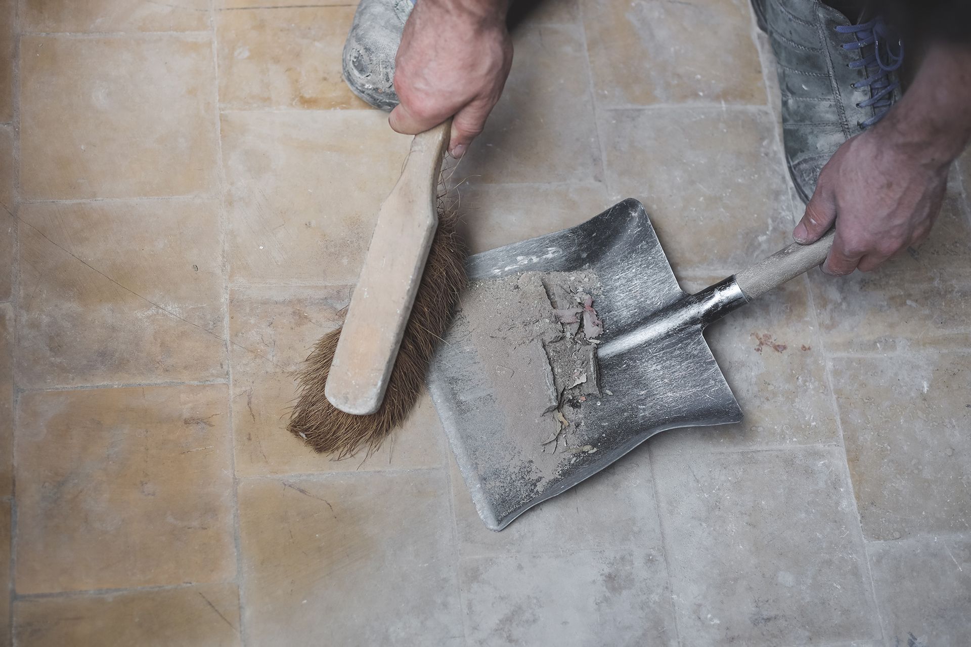 A person is cleaning the floor with a shovel and brush.