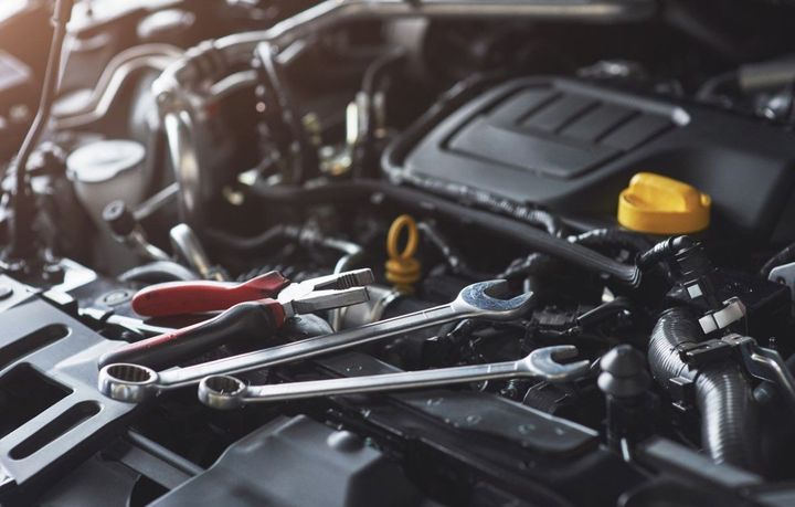 Car engine bay with tools on top, including a wrench and red-handled pliers, and a yellow oil cap