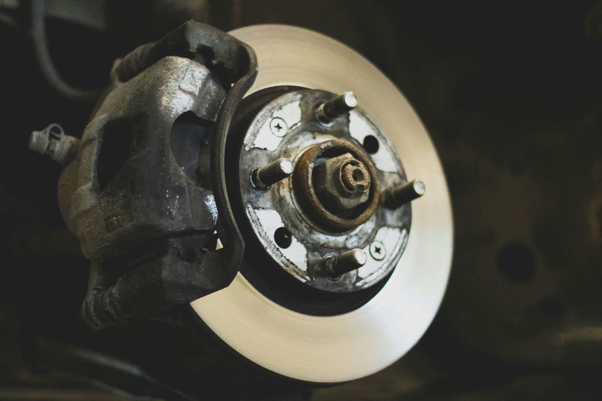 Car brake disc and caliper in close-up, with the wheel removed in a dark garage.