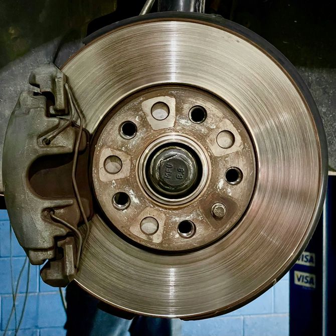 Car wheel brake disc and caliper assembly close-up, showing worn metal rotor and hub.