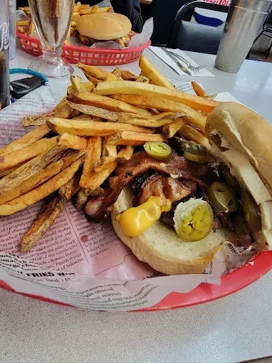 Burger with fries, bacon, and jalapenos on a red basket, served on a table in a diner.