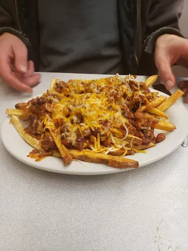 Plate of chili cheese fries; hands reach toward it on a diner table.