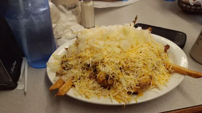 Plate of chili cheese fries with shredded cheese and onions.