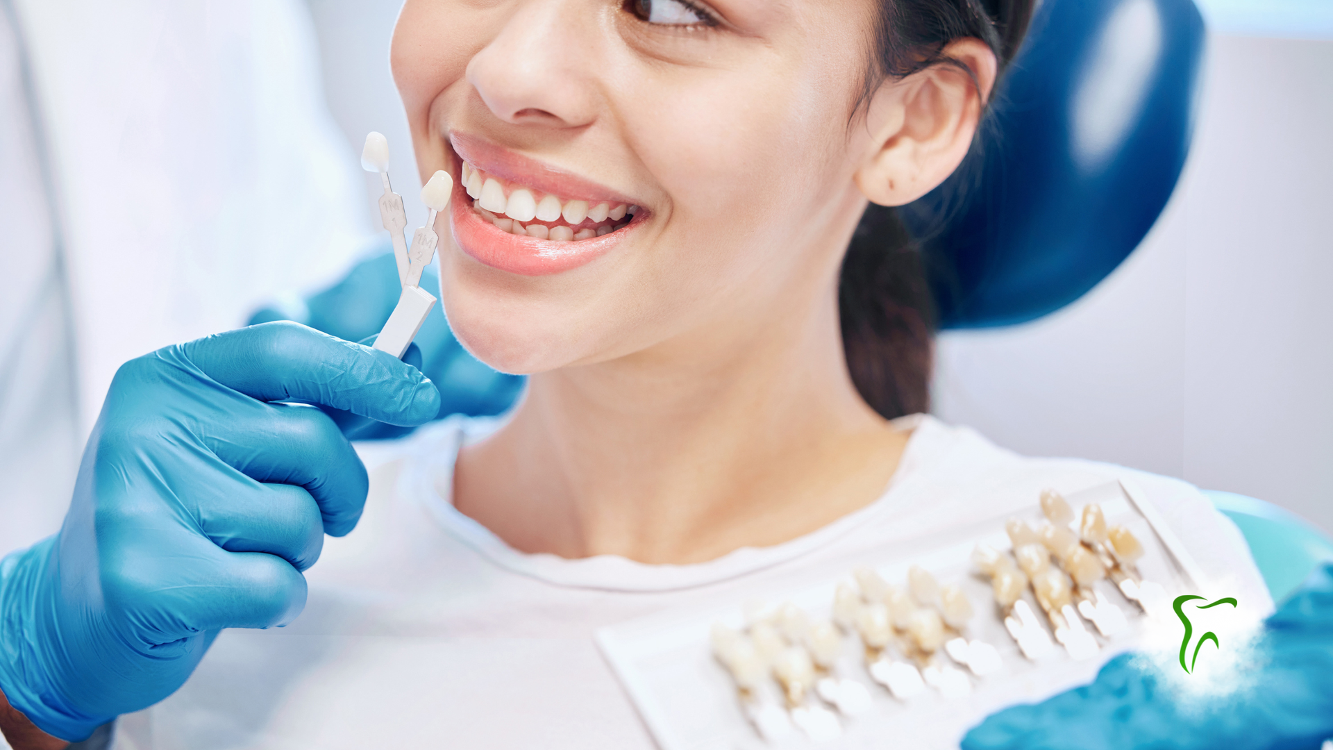 Dentist holding tooth shade guide next to patient's smile in a dental office.