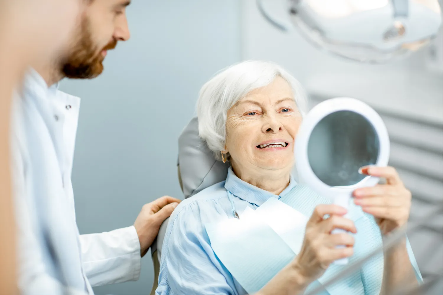 A woman is sitting in a dental chair while a dentist examines her teeth.