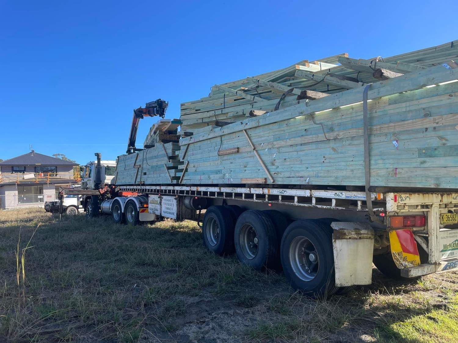 Truck Loaded With Lumber on a Grassy Lot, Crane Arm Extended, Blue Sky — McNamara's Frames & Trusses In Terrigal, NSW
